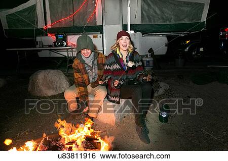 Stock Photograph - "Young couple sitting by camp-fire at night, laughing". Fotosearch