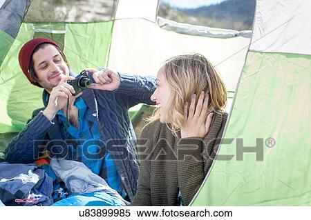 "Young couple sitting in tent, young man taking photograph of young woman with camera" View Large Photo Image Stock Photography - "Young couple sitting in tent, young man taking photograph of young woman with camera". Fotosearch