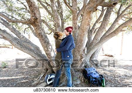 Stock Image - "Young couple standing in front of tree, embracing". Fotosearch
