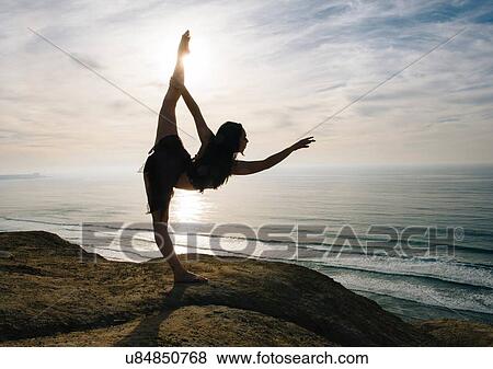 Stock Photo - "Young female dancer standing on rock, holding leg, stretching in elegant pose, San Diego, California, USA". Fotosearch