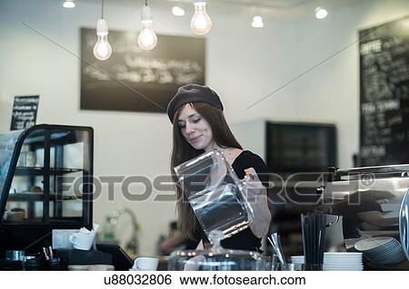 Stock Photograph - Young female waitress selecting cake at cafe counter. Fotosearch