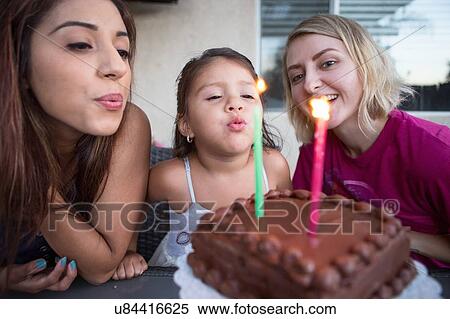 Stock Photography - "Young girl sitting with family, blowing out candles on birthday cake". Fotosearch