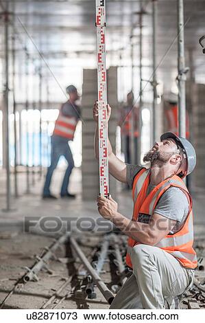 Stock Image - Young male builder measuring construction with ruler. Fotosearch