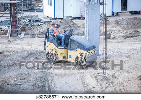 Stock Image - Young male labourer taking a break on steamroller at construction site. Fotosearch