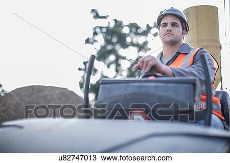 Stock Image - Young male steamroller driver on construction site. Fotosearch