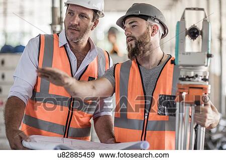 Young male surveyor explaining to site foreman on construction site View Large Photo Image Stock Photo - Young male surveyor explaining to site foreman on construction site. Fotosearch