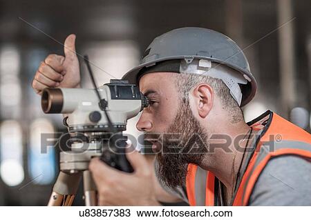 Young male surveyor looking through theodolite giving thumbs up on construction site View Large Photo Image Stock Image - Young male surveyor looking through theodolite giving thumbs up on construction site. Fotosearch