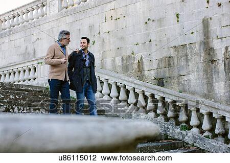 Stock Image - Young man and father chatting whilst moving down traditional stairway, Florence, Italy. Fotosearch