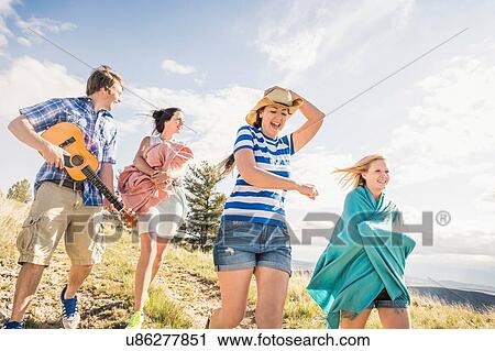 Stock Image - Young man and female friends playing ukulele whilst walking in hills, Bridger, Montana, USA. Fotosearch