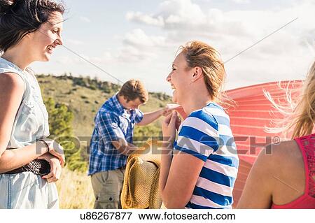 Stock Photo - Young man and female friends preparing picnic blanket on hillside, Bridger, Montana, USA. Fotosearch