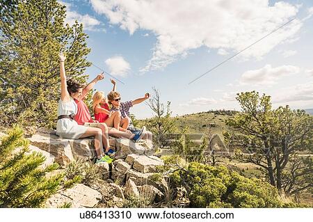Stock Image - Young man and friends taking selfie sitting on rocks, Bridger, Montana, USA. Fotosearch