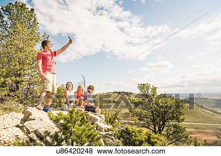 Stock Photo - Young man and friends taking smartphone selfie on rocks, Bridger, Montana, USA. Fotosearch