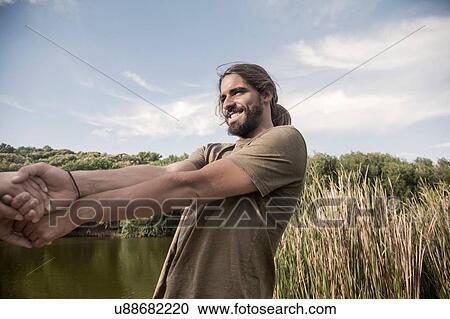 Young man by river holding hands, leaning back smiling View Large Photo Image Stock Image - Young man by river holding hands, leaning back smiling. Fotosearch