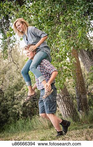Picture - Young man carrying teenage girl on shoulders in rural woods. Fotosearch