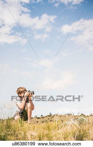 Stock Photo - Young man crouching to photograph landscape, Bridger, Montana, USA. Fotosearch