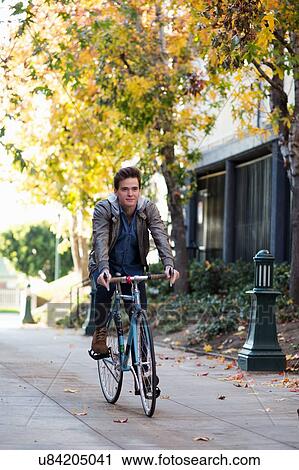 Stock Image - Young man cycling along sidewalk. Fotosearch