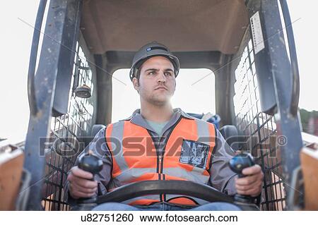 Stock Image - Young man driving excavator on construction site. Fotosearch