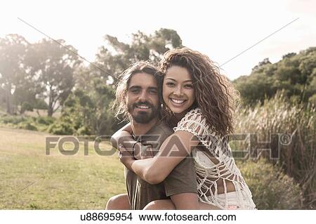 Young man giving young woman piggyback looking at camera smiling View Large Photo Image Picture - Young man giving young woman piggyback looking at camera smiling. Fotosearch