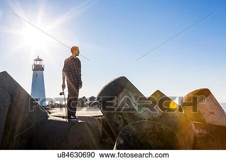 "Young man holding skateboard, standing on breakwater near lighthouse, looking towards ocean" View Large Photo Image Stock Image - "Young man holding skateboard, standing on breakwater near lighthouse, looking towards ocean". Fotosearch