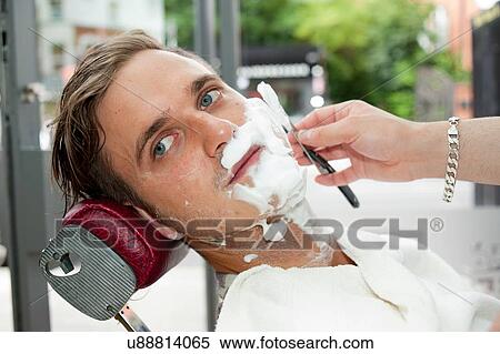 Young man in barbershop, face covered in shaving cream being shaved with straight razor looking away View Large Photo Image Stock Photography - Young man in barbershop, face covered in shaving cream being shaved with straight razor looking away. Fotosearch
