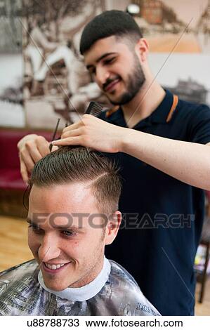 Stock Image - Young man in barbershop having haircut, smiling. Fotosearch