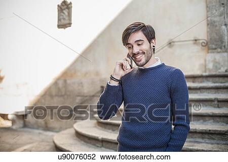 Stock Image - Young man in front of stone steps using smartphone smiling. Fotosearch