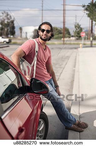 Young man leaning against red car at roadside, Los Angeles, California, USA View Large Photo Image Stock Image - Young man leaning against red car at roadside, Los Angeles, California, USA. Fotosearch