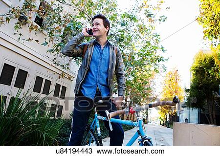 Young man on cycle chatting on smartphone View Large Photo Image Stock Image - Young man on cycle chatting on smartphone. Fotosearch