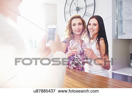 Young man photographing female friends on smartphone in kitchen View Large Photo Image Stock Photo - Young man photographing female friends on smartphone in kitchen. Fotosearch
