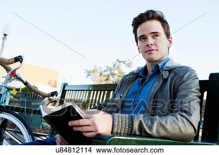 Young man reading book on park bench View Large Photo Image Picture - Young man reading book on park bench. Fotosearch