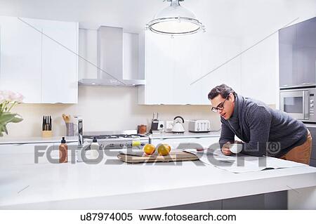 Young man reading newspaper at kitchen counter View Large Photo Image Stock Photography - Young man reading newspaper at kitchen counter. Fotosearch