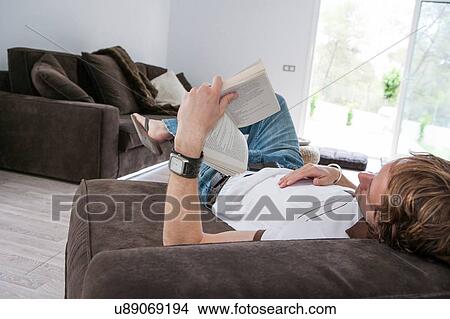 Young man reclining on sofa reading a book View Large Photo Image Picture - Young man reclining on sofa reading a book. Fotosearch