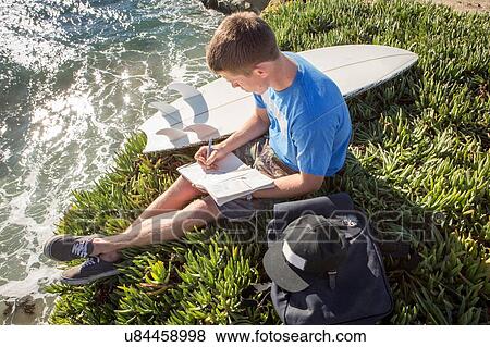 "Young man sitting by cliff edge, writing in book, elevated view" View Large Photo Image Stock Photo - "Young man sitting by cliff edge, writing in book, elevated view". Fotosearch