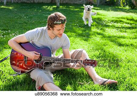 Young man sitting in garden playing acoustic guitar View Large Photo Image Stock Photo - Young man sitting in garden playing acoustic guitar. Fotosearch