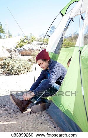 "Young man sitting in tent, putting on boots" View Large Photo Image Stock Image - "Young man sitting in tent, putting on boots". Fotosearch