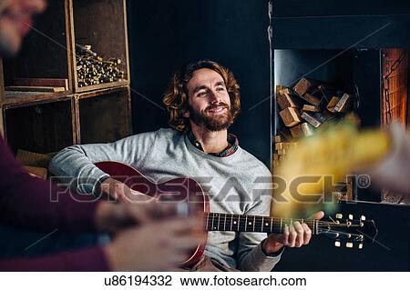 Young man sitting on floor playing guitars in living room View Large Photo Image Stock Image - Young man sitting on floor playing guitars in living room. Fotosearch