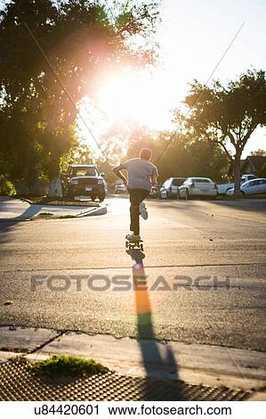 Stock Image - "Young man skateboarding in road, rear view, Corona, California, USA". Fotosearch