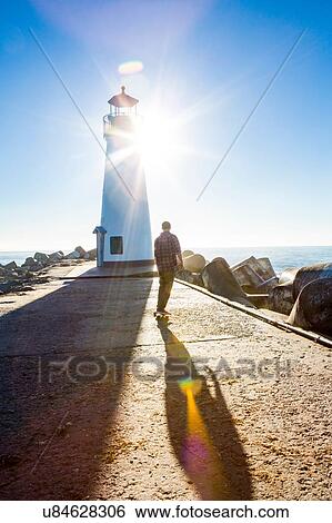 Stock Photograph - "Young man skating on skateboard, near lighthouse, rear view". Fotosearch