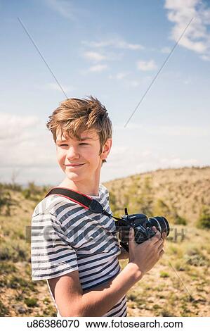 Stock Image - Young man with camera looking over his shoulder, Bridger, Montana, USA. Fotosearch