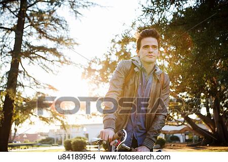 Picture - Young man with cycle waiting and looking away. Fotosearch