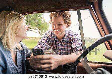 Stock Image - Young man with girlfriend reading smartphone texts at jeep window. Fotosearch