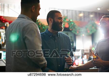 Young men in public house holding beer bottles leaning against counter smiling View Large Photo Image Stock Photo - Young men in public house holding beer bottles leaning against counter smiling. Fotosearch