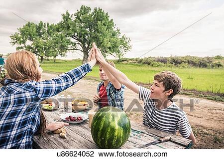 Young woman and friends giving high five at picnic table View Large Photo Image Stock Image - Young woman and friends giving high five at picnic table. Fotosearch