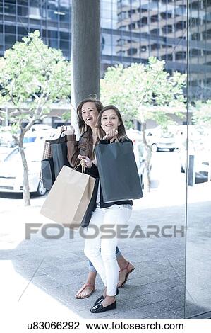 Stock Image - Young woman and teenage girl carrying shopping bags in city. Fotosearch