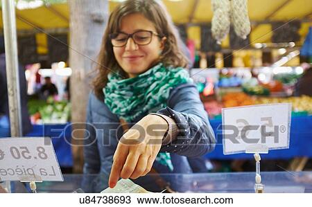Stock Image - Young woman buying goods at market stall. Fotosearch