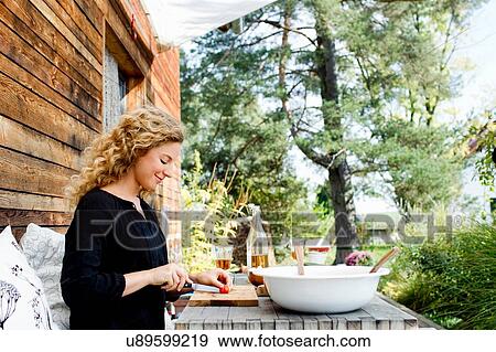 Stock Photo - Young woman chopping vegetables at table outdoors. Fotosearch