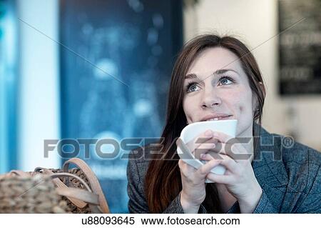 Young woman drinking coffee in cafe looking up View Large Photo Image Stock Photography - Young woman drinking coffee in cafe looking up. Fotosearch
