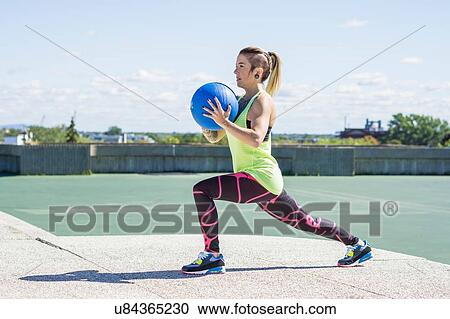 Stock Image - "Young woman exercising with ball, outdoors". Fotosearch