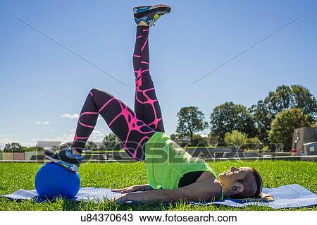 Stock Image - "Young woman exercising with ball, outdoors". Fotosearch