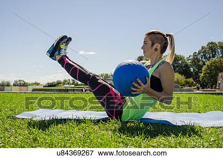 Stock Photo - "Young woman exercising with ball, outdoors". Fotosearch